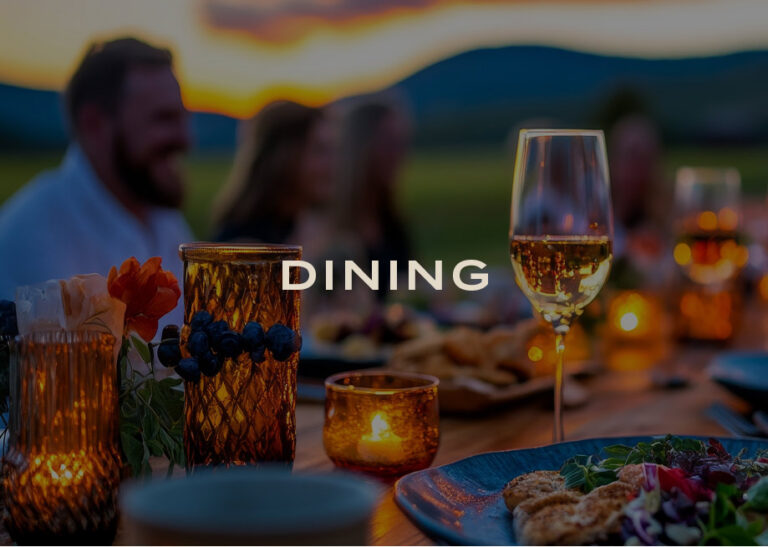 Dining: an outdoor sunset dinner table with candles and wine, guests in the background