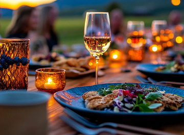 A candlelit outdoor dinner table with wine and a shared meal at sunset